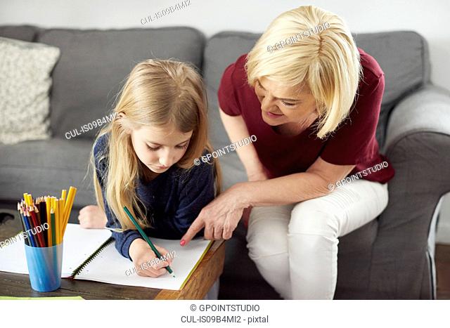 Grandmother helping granddaughter with colouring at home