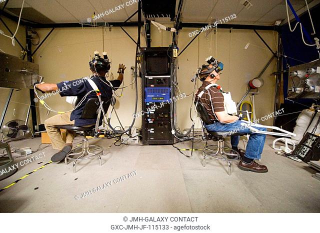 NASA astronauts Alvin Drew (left) and Tim Kopra, both STS-133 mission specialists, use virtual reality hardware in the Space Vehicle Mock-up Facility at NASA's...