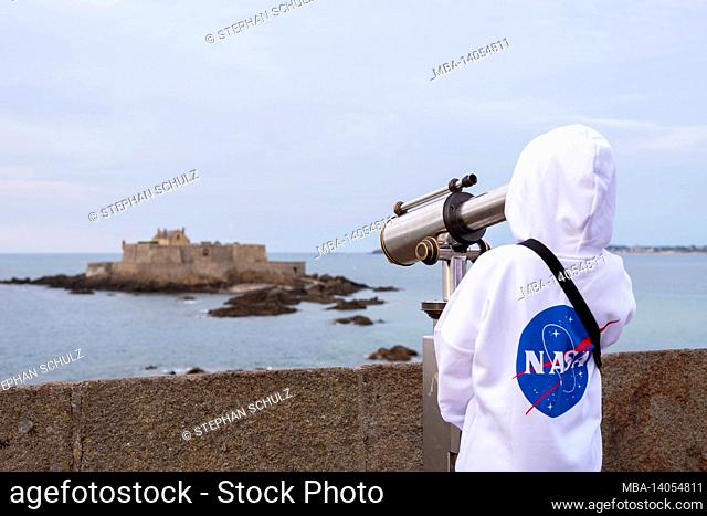 france, brittany, ille et vilaine, saint malo, boy looks through a telescope to the tidal island of petit-bé with the fort national, atlantic coast
