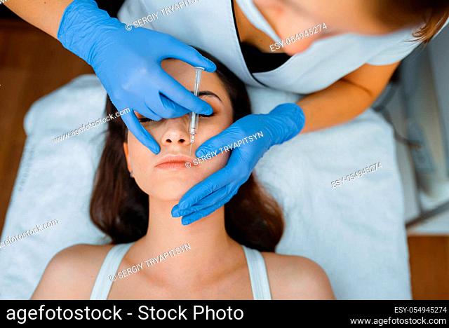 Cosmetician in gloves gives face botox injections to female patient on treatment table. Rejuvenation procedure in beautician salon