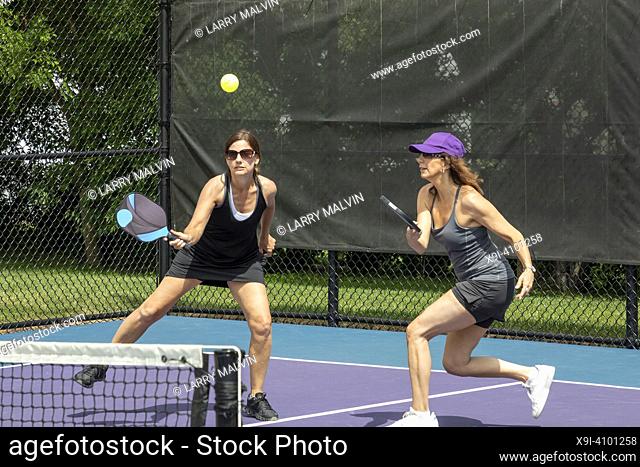 Two pickleball players prepare to return a ball on a suburban pickleball court during summer