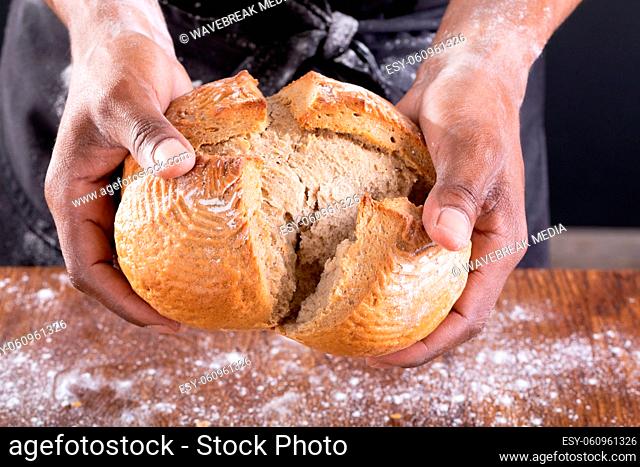 Midsection of african american male baker breaking bread over table