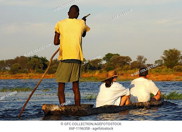 Poler with tourists in a traditional mokoro logboat on excursion in the Okavango Delta, Botswana