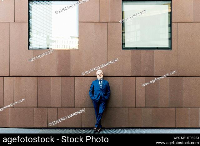 Senior businessman standing with hands in pockets outside building exterior