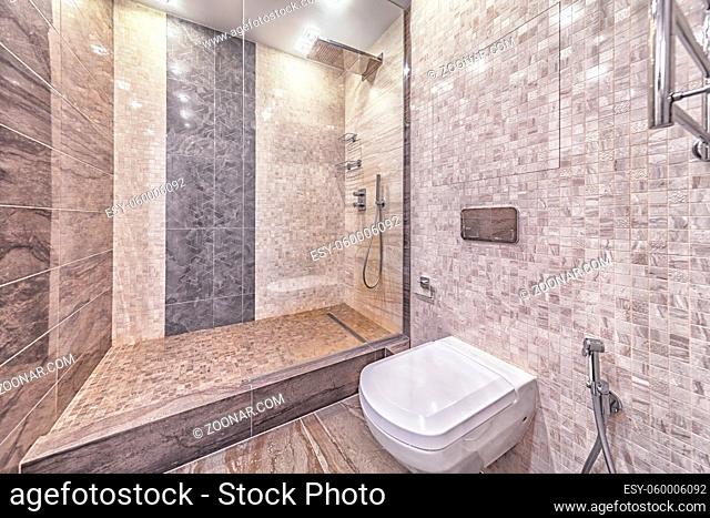 Modern tiled bathroom interior: build in toilet seat and transparent glass shower door