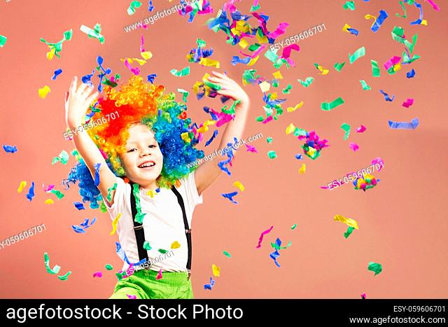 Little boy in clown wig jumping and having fun celebrating birthday. Portrait of a child throws up a multi-colored tinsel and confetti. Birthday boy