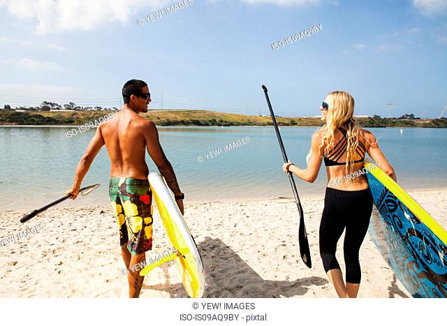Couple carrying paddleboards on beach, Carlsbad, California, USA