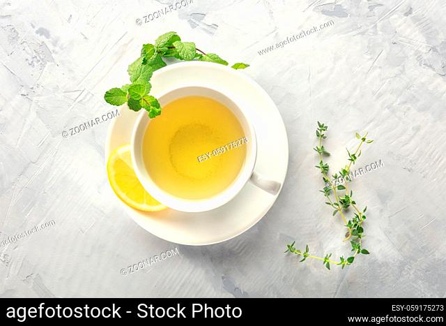 A cup of green tea with lemon, shot from above with mint, thyme, and copy space