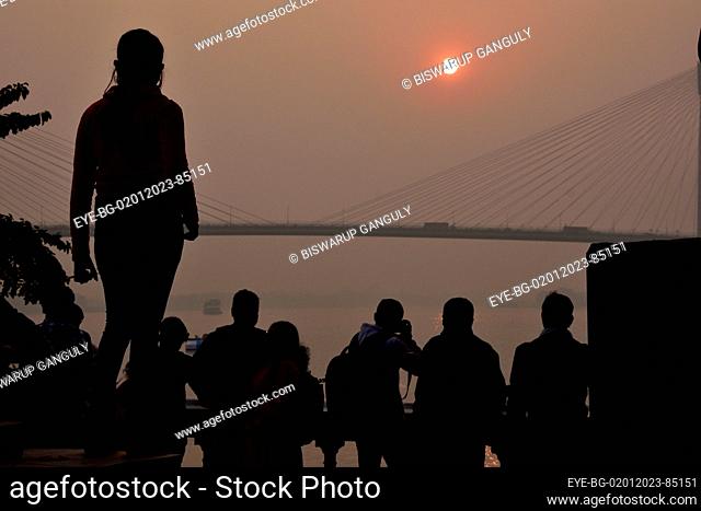 Dec 31, 2022, Kolkata, India. Persons enjoy the sunset across the  Howrah Bridge (Vidyasagar Setu) On River Ganges. scenic beauty of the setting sun on the last...