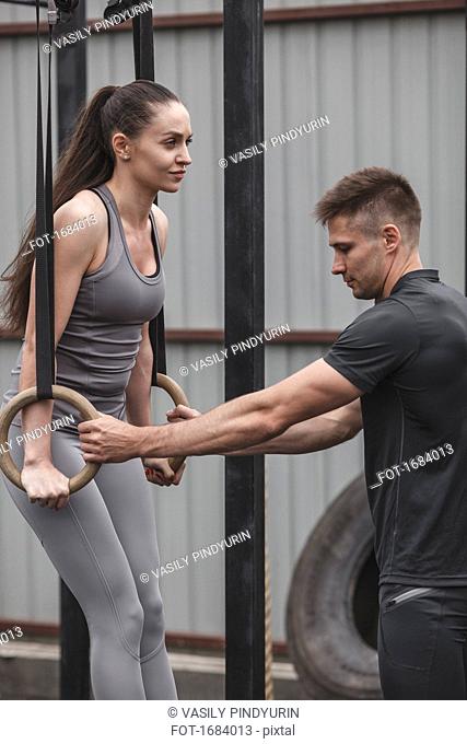 Male instructor assisting female athlete exercising on gymnastic rings during crossfit training