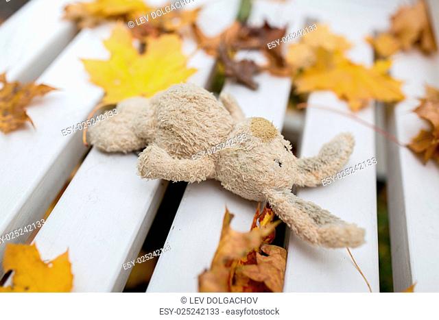 season, childhood and loneliness concept - lonely toy rabbit on bench in autumn park