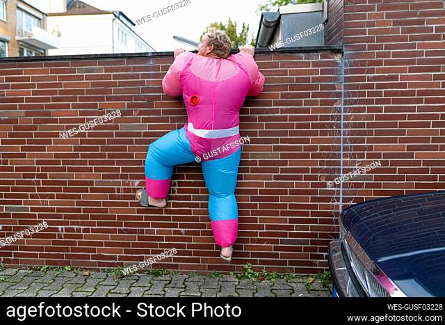 Man wearing pink bodybuilder costume climbing over a wall
