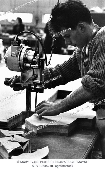 Man at work in a clothing factory in Hemel Hempstead, cutting multiple pieces of cloth