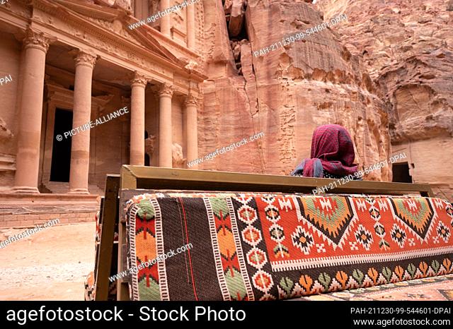 21 November 2021, Jordan, Petra: A woman wearing a headscarf sits in front of the Al Khazneh treasure house in the ancient Nabataean city of Petra
