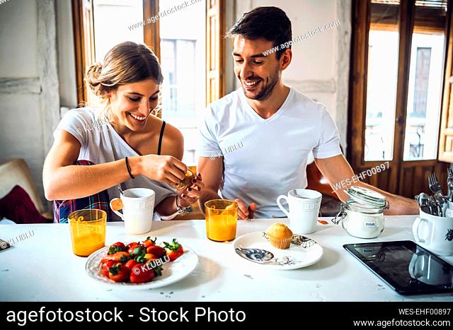 Happy young couple sitting at table and having breakfast at home