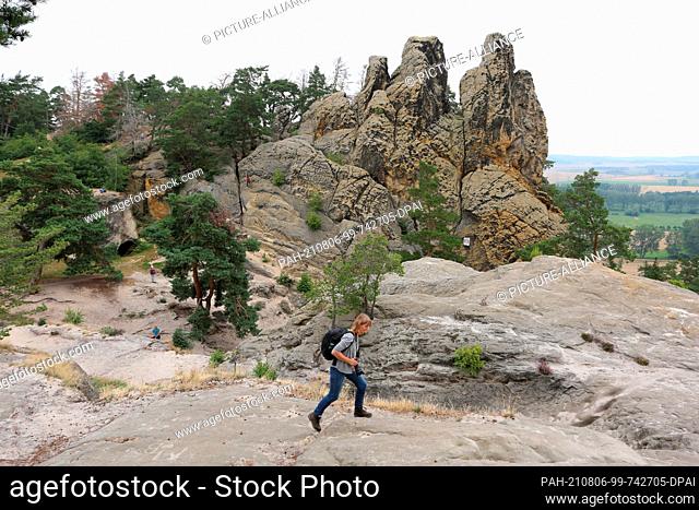 05 August 2021, Saxony-Anhalt, Timmenrode: A hiker walks along the path leading over the Devil's Wall to Blankenburg to the rock formation ""Drei Zinnen""