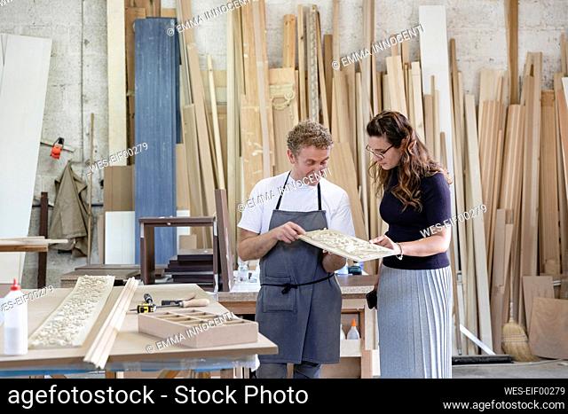 Female inspector and carpenter discussing inlay work while standing at workshop