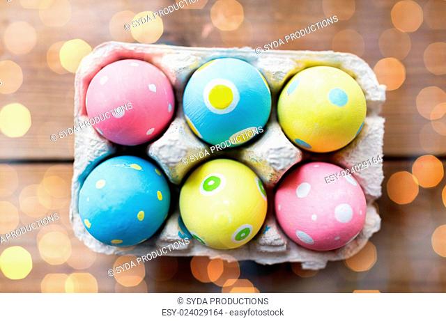 easter, holidays, tradition and object concept - close up of colored easter eggs in egg box or carton wooden surface