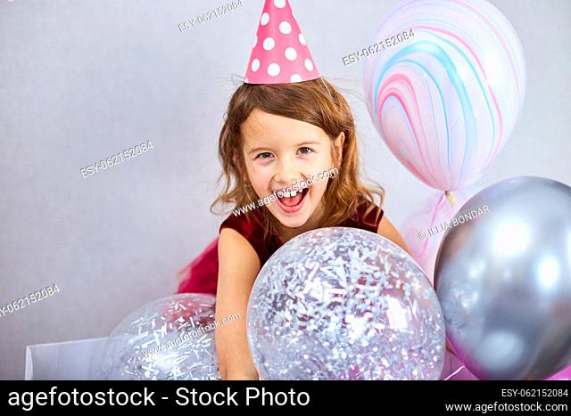 Cute, Joyful little girl in pink dress and hat play with balloons at home birthday party streamers, Happy birthday. Celebrating