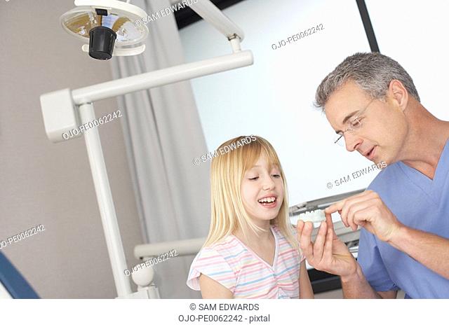 Dentist in examination room showing smiling young patient mold of teeth