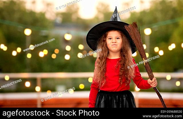 girl in black witch hat with broom on halloween