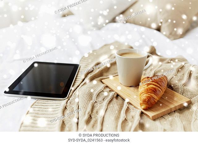 tablet pc, coffee and croissant on bed at home