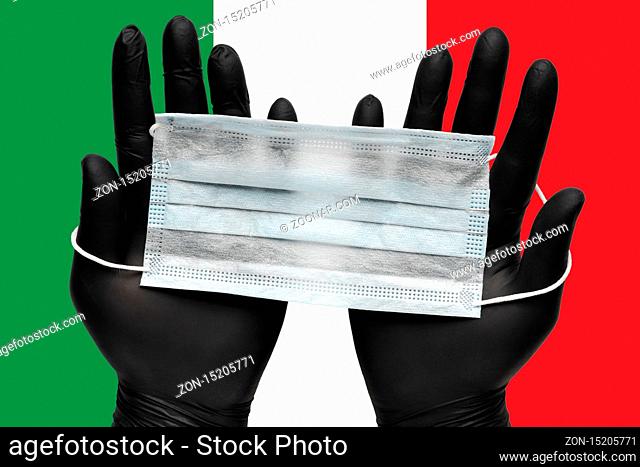 Doctor holds face mask in hands in black medical gloves on background colors flag of Italy or Italian Tricolour. Pandemic insurance coronavirus, flu