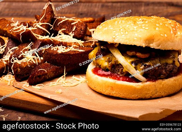 Delicious cheeseburger with cheese, fresh lettuce, onion and tomato on a fresh bun with sesame seed and toast standing on brown paper on a wooden background
