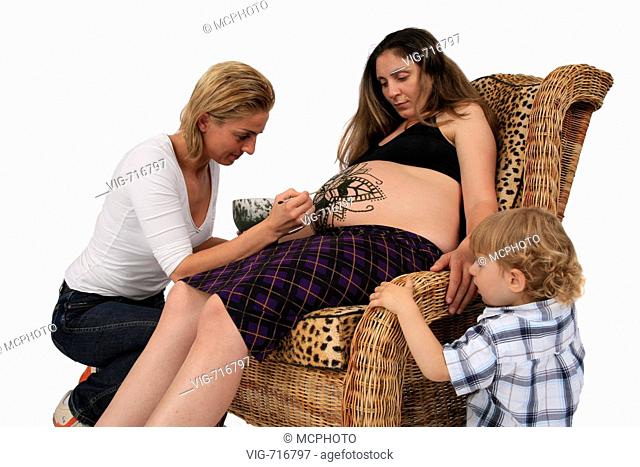young woman is painting henna-tattoo on pregnant belly, Germany  - GERMANY, 03/09/2007