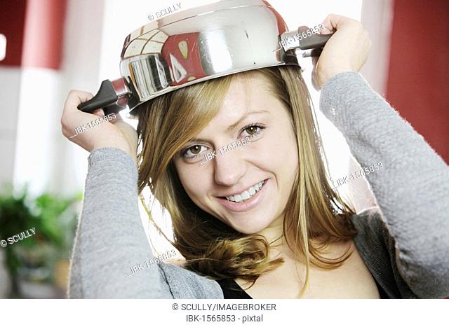 Young woman in a kitchen using a cooking pot as a hat