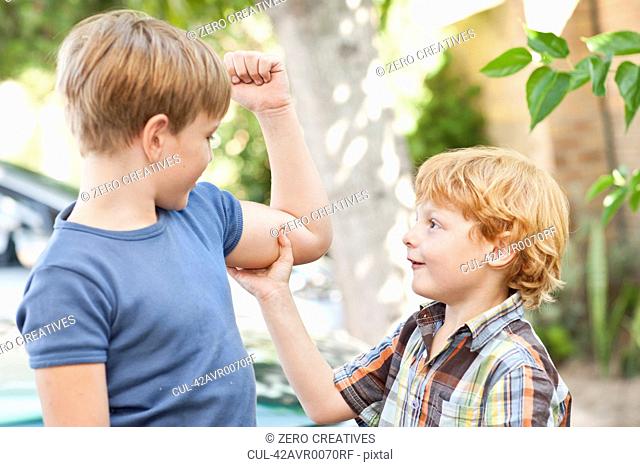 Boy feeling brothers biceps outdoors