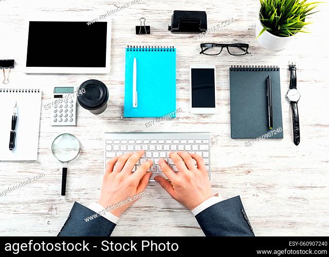 Businessman typing at computer keyboard at wooden desk. Well organized office workspace with digital gadgets. Business occupation concept with man in business...