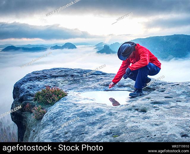 Nice hiker girl on mountain summit soak maple leaf in water eye pool