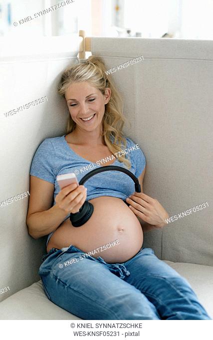 Smiling pregnant woman holding headphones at her belly