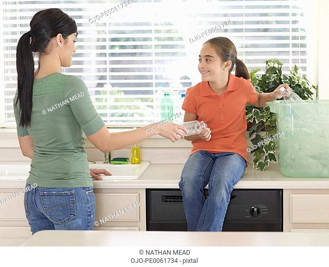Woman and young girl in kitchen recycling plastic bottles and smiling