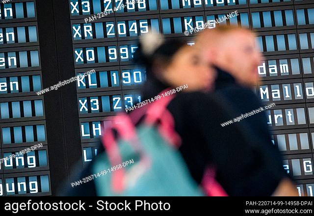 14 July 2022, Lower Saxony, Hanover: People wait in front of a display board in the departure hall of Terminal A at Hannover Airport