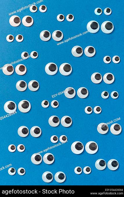 Googly plastic eyes pattern of clear, hard-plastic shell with a small black plastic disk different sizes on a blue background. Flat lay