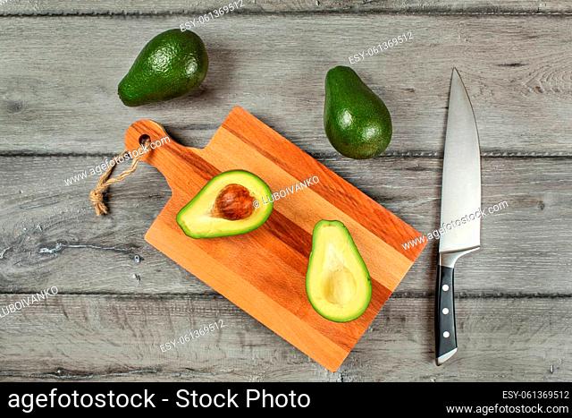 Tabletop view, avocado cut in half, seed visible, on a chopping board, chef knife, and two whole green pears next to in