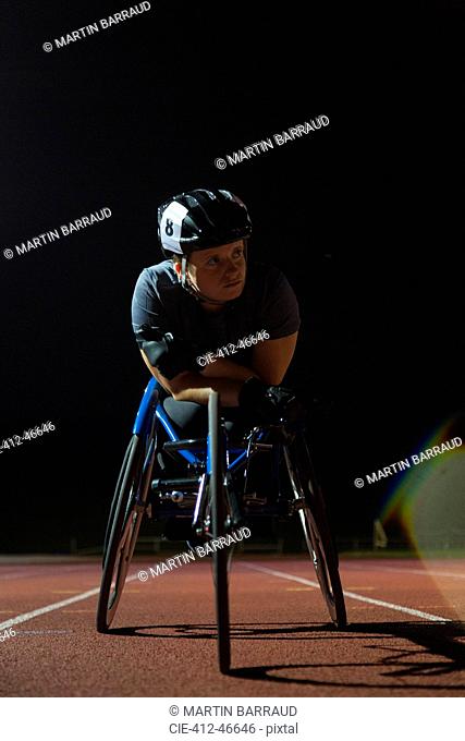 Determined young female paraplegic athlete training for wheelchair race on sports track at night