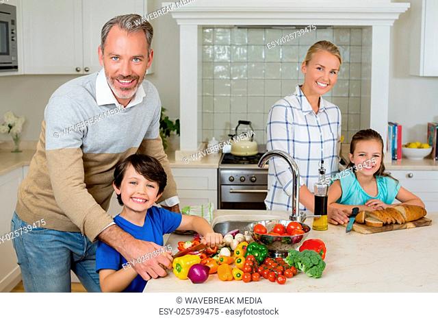 Smiling parents assisting a kids to chop vegetables in kitchen