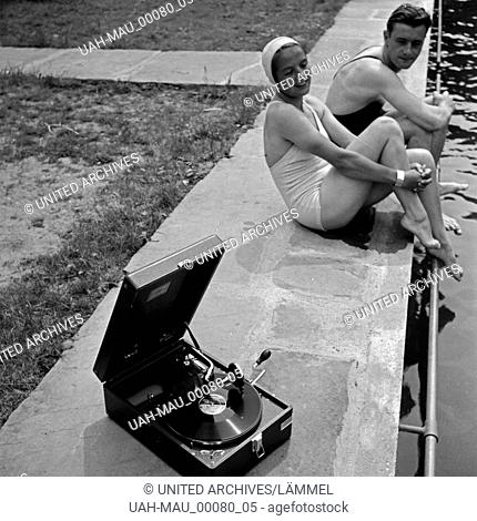 Ein junges Paar sitzt im Freibad am Beckenrand und hört die neuesten Schlager auf einem Elextrole Grammophon, Deutschland 1930er Jahre