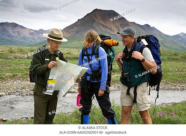Native Indian National Park Service Ranger talks and shows map to couple along the Toklat River Denali NP Alaska