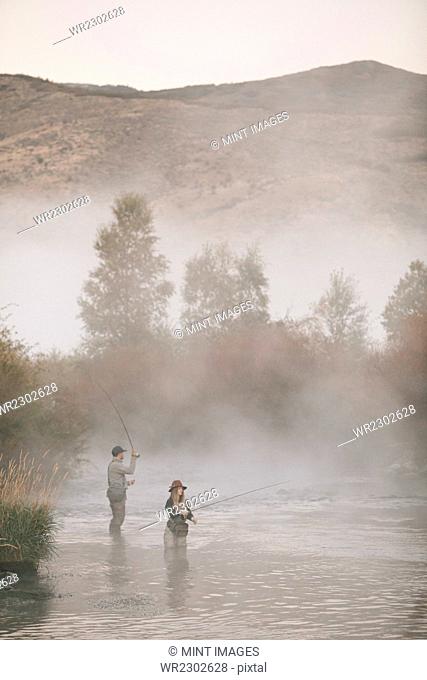 A couple, a man and woman standing in mid stream fly fishing in a river
