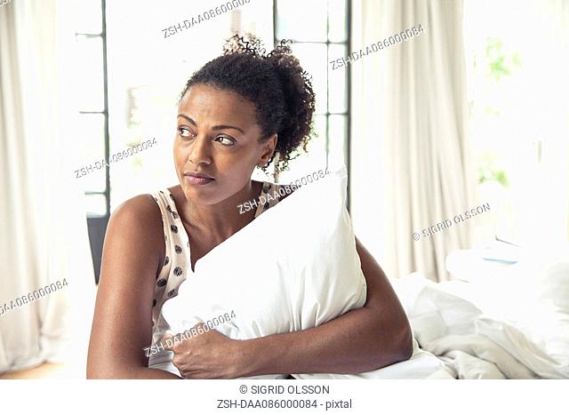 Woman hugging pillow on bed, portrait
