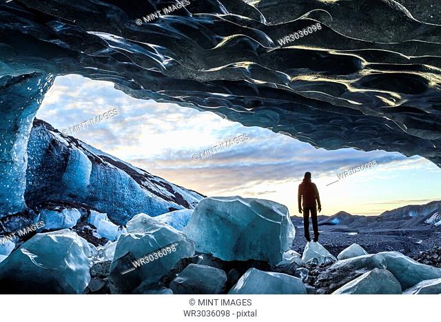 Rear view silhouette of person standing on ice rock at the entrance to a glacial ice cave