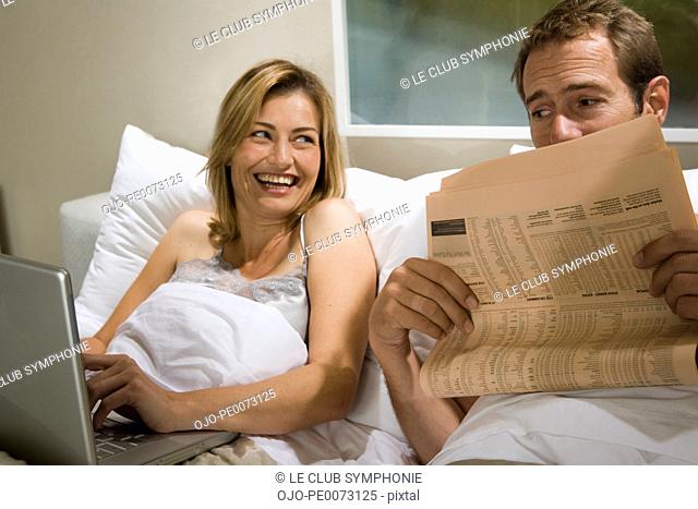 Couple in bed with laptop and newspaper