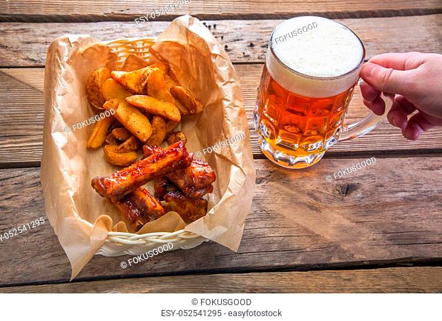 Mug of beer in hand and a plate with a beer snack on a wooden table