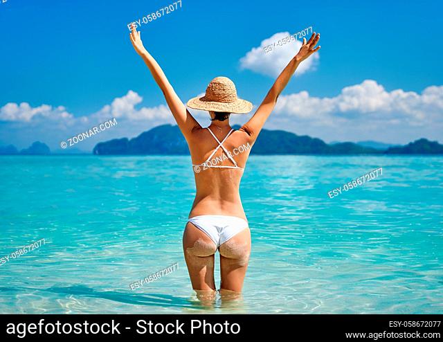 Rear view of a beautiful happy girl with raised hands enjoy her tropical beach vacation. Summer relax, travel destination