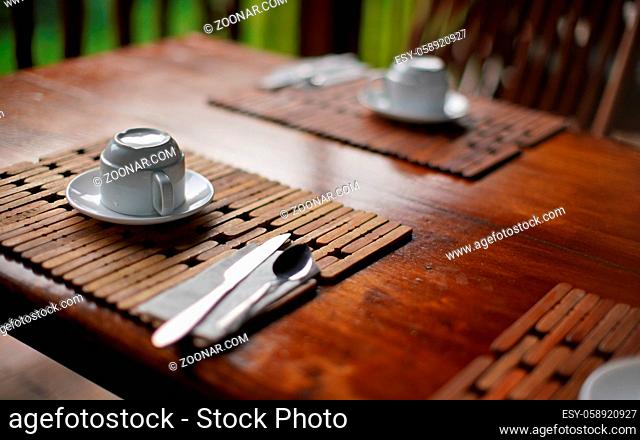 Shallow depth of field detail photo of empty coffee cup upside down on wooden table desk, morning breakfast in tropical holiday resort