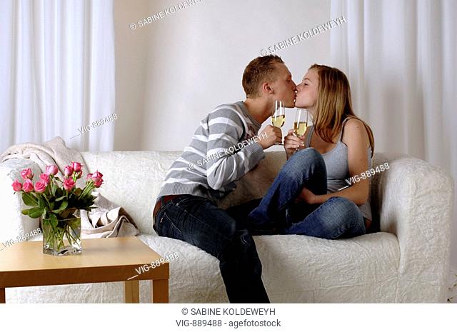Young couple sitting kissing on a sofa and drinking sparkling wine. - 30/06/2008